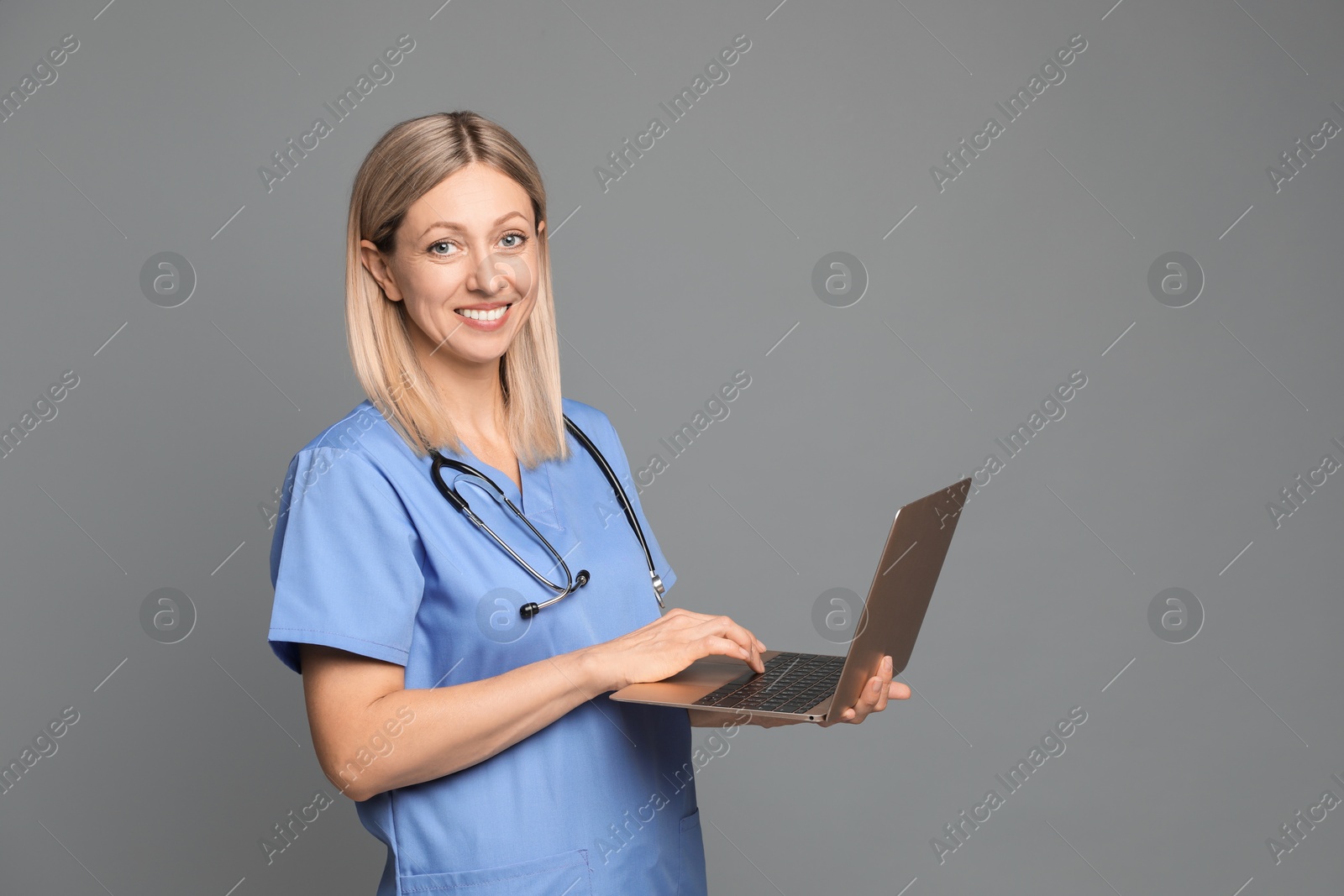 Photo of Doctor in medical uniform with stethoscope using laptop on grey background