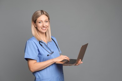 Doctor in medical uniform with stethoscope using laptop on grey background