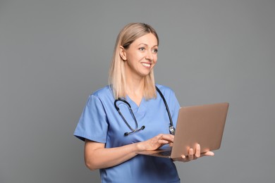 Photo of Doctor in medical uniform with stethoscope using laptop on grey background