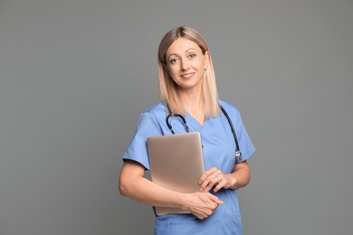 Photo of Doctor in medical uniform with stethoscope and laptop on grey background