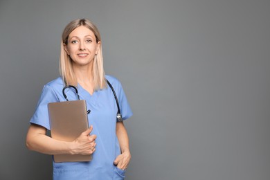 Doctor in medical uniform with stethoscope and laptop on grey background, space for text