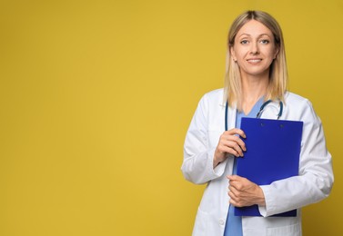 Portrait of doctor in medical uniform with stethoscope and clipboard on yellow background, space for text