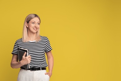 Photo of Beautiful smiling woman with notebooks on yellow background, space for text