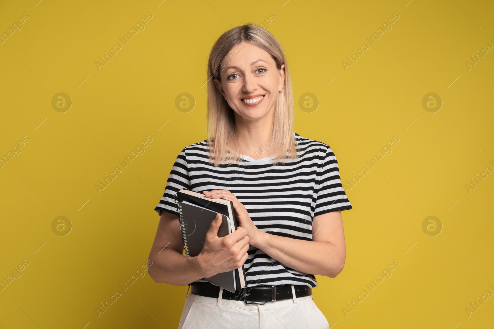 Photo of Beautiful smiling woman with notebooks on yellow background