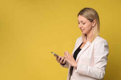 Photo of Beautiful smiling woman using smartphone on yellow background, space for text