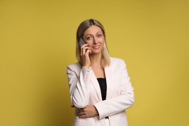 Beautiful smiling woman talking on smartphone against yellow background