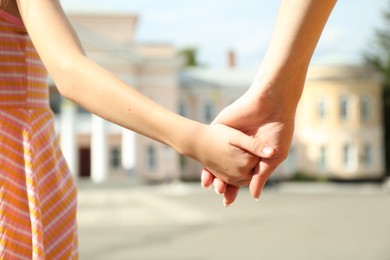 Photo of Mother and daughter holding hands outdoors, closeup