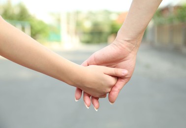 Photo of Mother and daughter holding hands outdoors, closeup