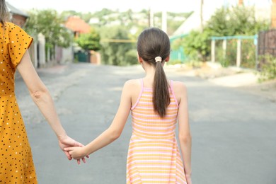 Photo of Little girl holding hands with mother outdoors, back view