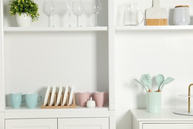 Shelving unit with different kitchenware near white wall indoors