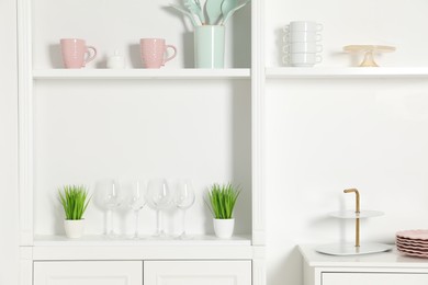 Shelving unit with different kitchenware near white wall indoors