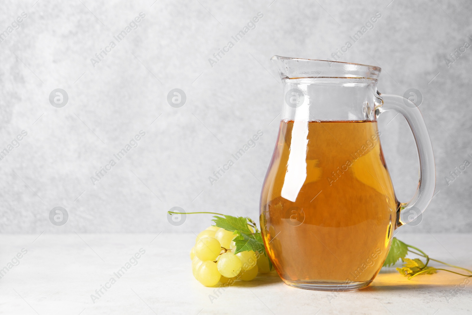 Photo of Tasty grape juice in jar and berries on light table. Space for text