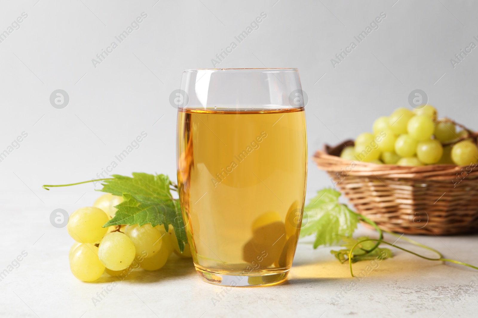 Photo of Tasty grape juice in glass, leaves and berries on light table, closeup