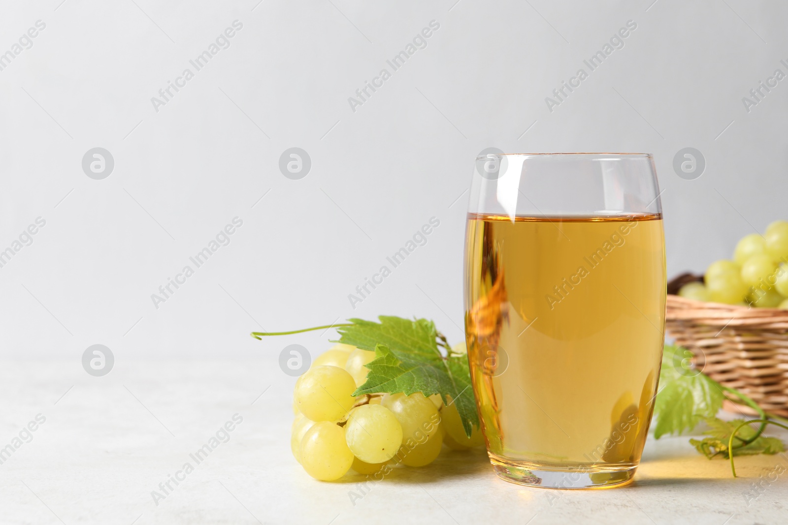 Photo of Tasty grape juice in glass, leaves and berries on light table, closeup. Space for text