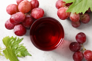 Photo of Tasty grape juice in glass, leaves and berries on light table, flat lay