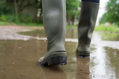 Photo of Woman wearing green rubber boots walking in puddle outdoors, closeup. Space for text