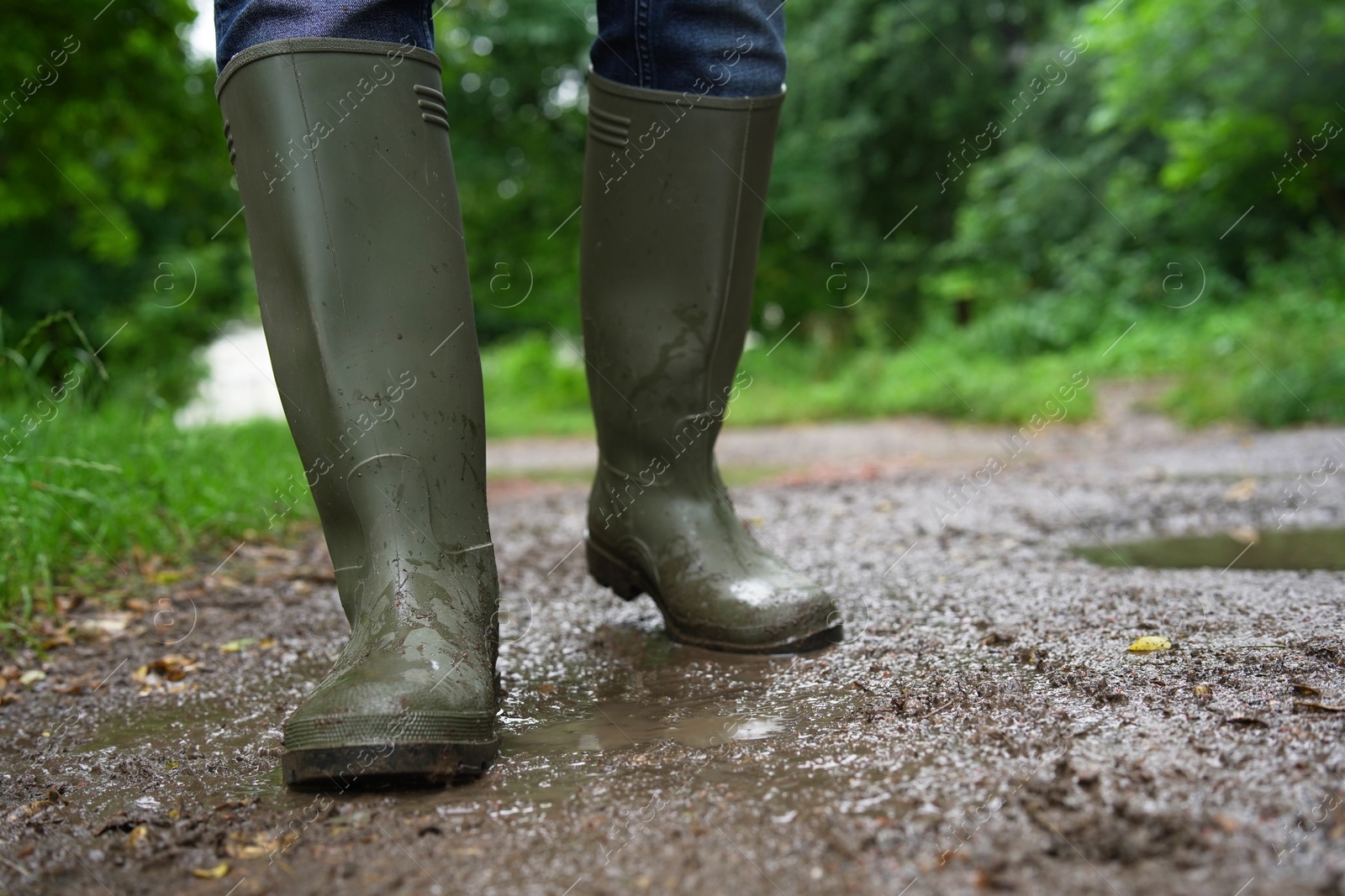 Photo of Woman in green rubber boots walking on muddy road, closeup. Space for text