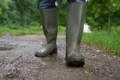 Photo of Woman in green rubber boots walking on muddy road, closeup