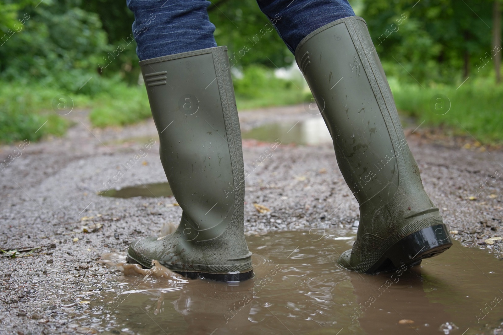 Photo of Woman wearing green rubber boots walking in puddle outdoors, closeup