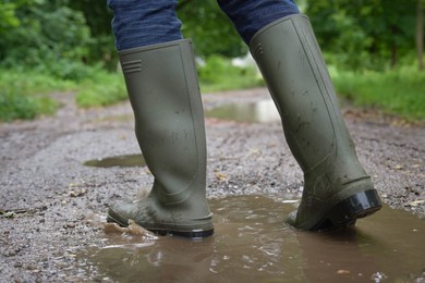 Woman wearing green rubber boots walking in puddle outdoors, closeup