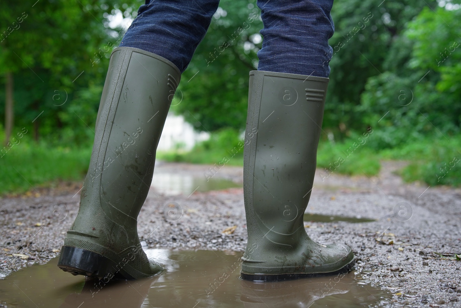 Photo of Woman wearing green rubber boots walking in puddle outdoors, closeup