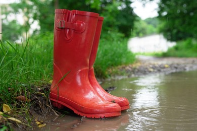 Photo of Red rubber boots in puddle at rainy day, closeup