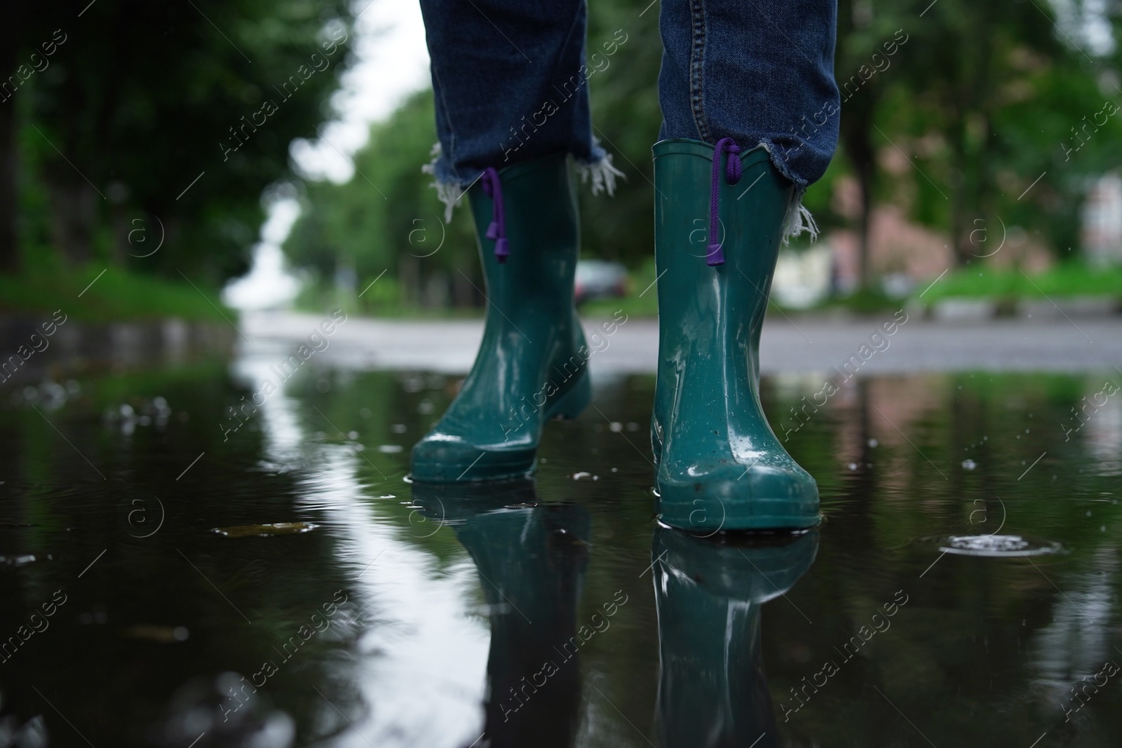 Photo of Woman wearing turquoise rubber boots walking in puddle outdoors, closeup. Space for text