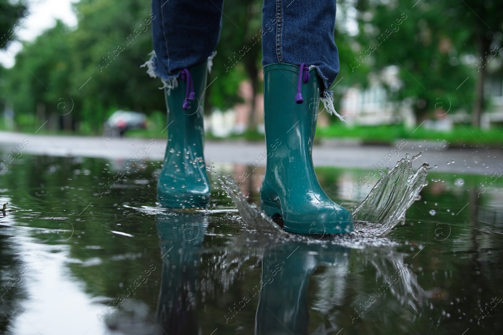 Photo of Woman wearing turquoise rubber boots walking in puddle outdoors, closeup