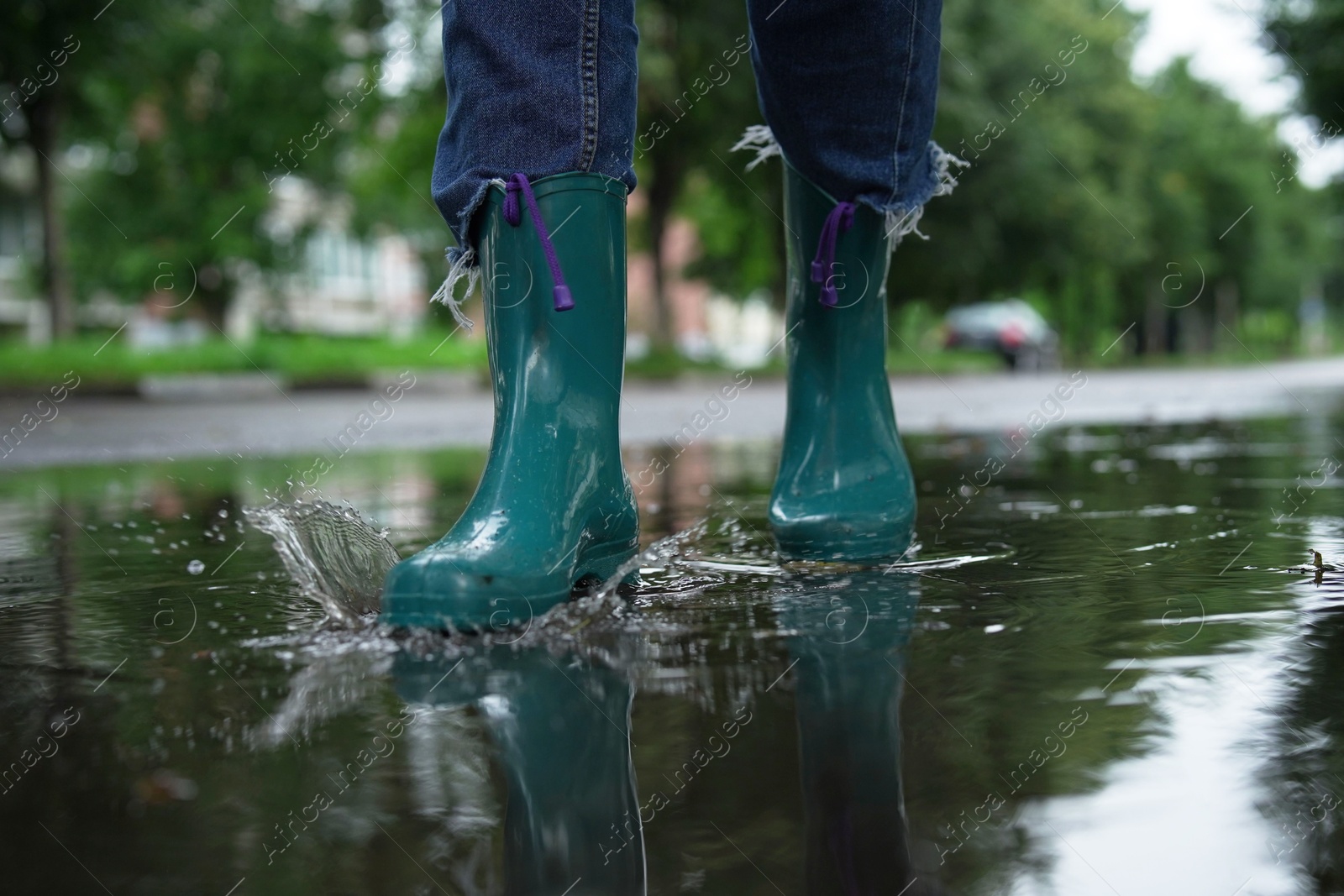 Photo of Woman wearing turquoise rubber boots walking in puddle outdoors, closeup