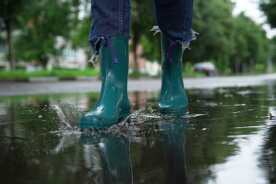 Woman wearing turquoise rubber boots walking in puddle outdoors, closeup