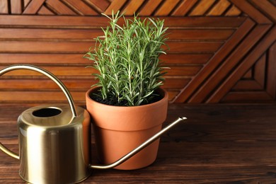 Photo of Aromatic rosemary plant in pot and watering can on wooden table, space for text