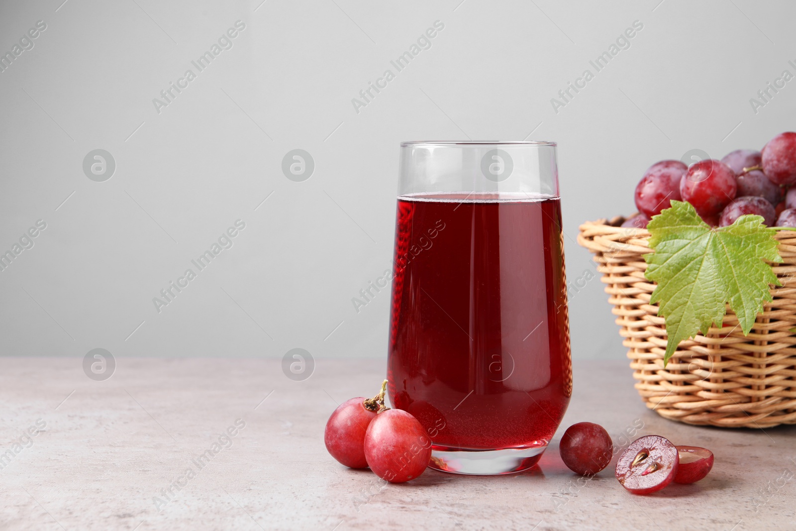 Photo of Ripe grapes and glass of tasty juice on grey table. Space for text