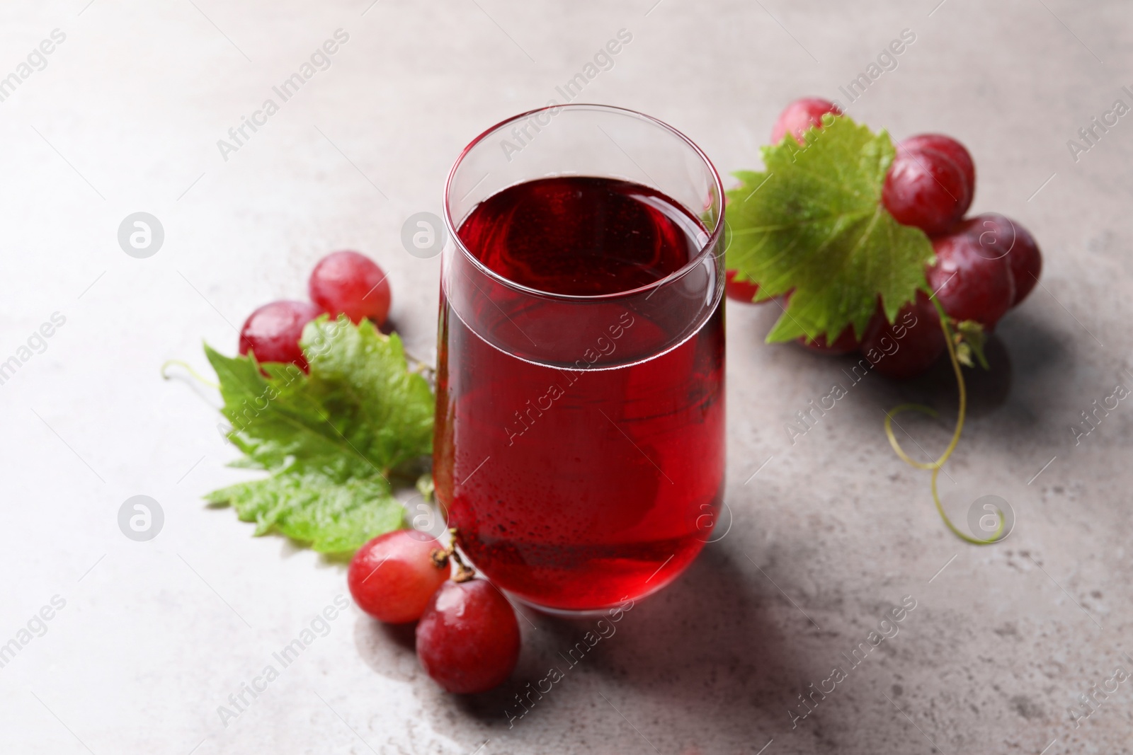 Photo of Ripe grapes and glass of tasty juice on grey table