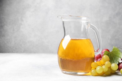 Photo of Ripe grapes and jug of tasty juice on grey table. Space for text