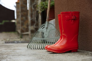 Photo of Orange rubber boots and rake near wall outdoors