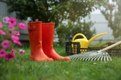 Photo of Orange rubber boots and gardening tools on green grass outdoors