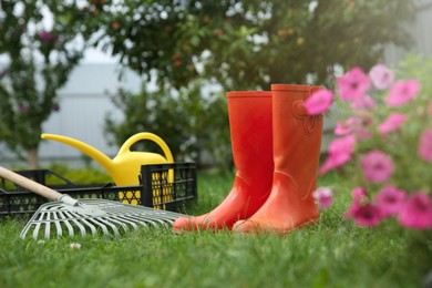 Orange rubber boots and gardening tools on green grass outdoors