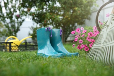 Photo of Rubber boots, gardening tools and petunia flowers on green grass outdoors