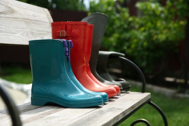 Photo of Three pairs of rubber boots on wooden bench outdoors