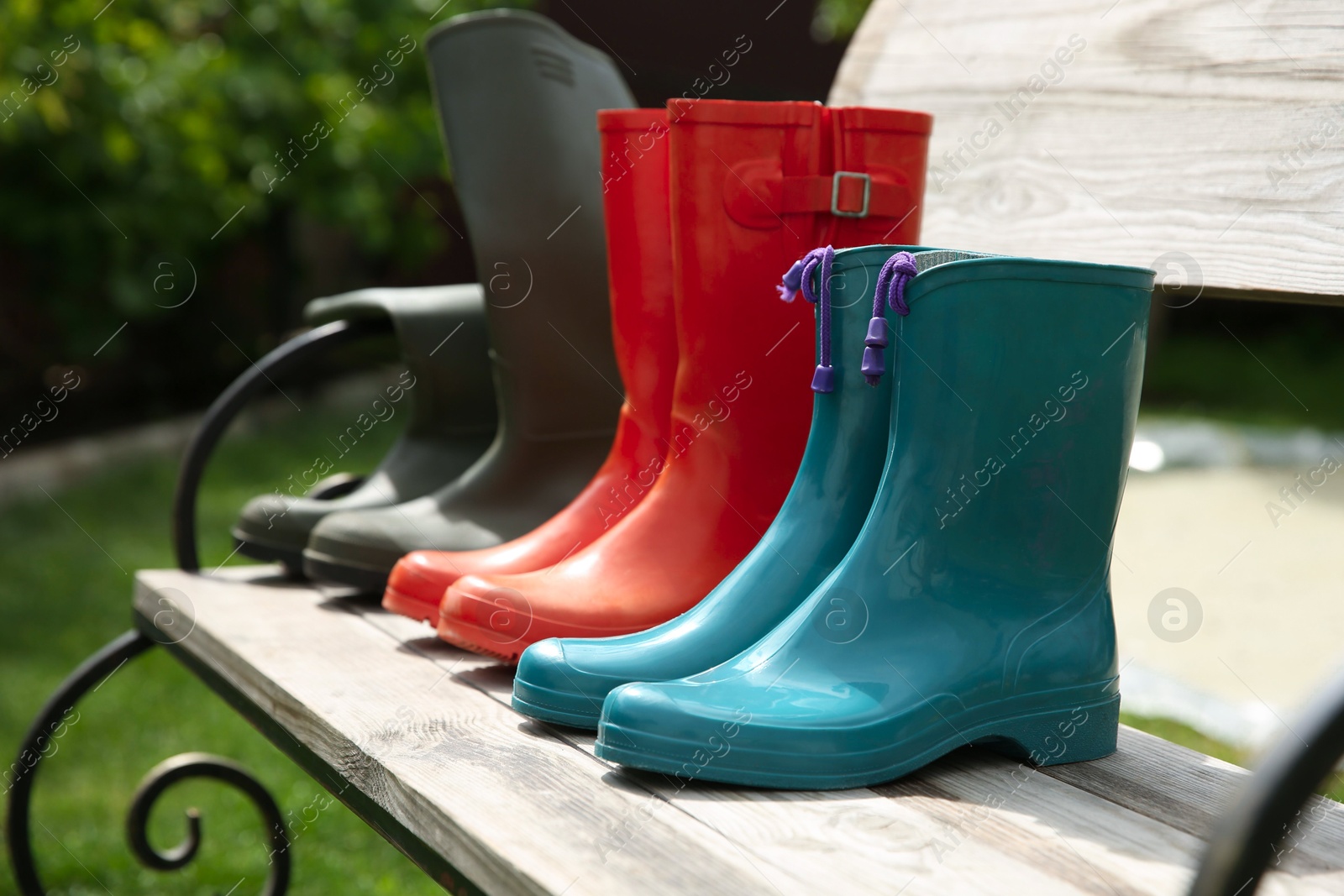 Photo of Three pairs of rubber boots on wooden bench outdoors