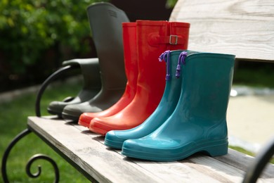 Photo of Three pairs of rubber boots on wooden bench outdoors