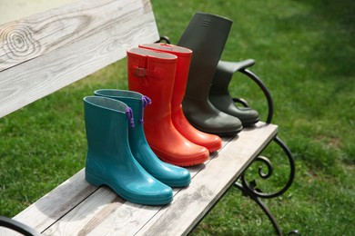 Three pairs of rubber boots on wooden bench outdoors