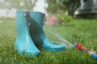 Photo of Bright rubber boots under water pressure on green grass outdoors