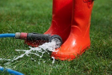 Photo of Orange rubber boots under water pressure on green grass outdoors