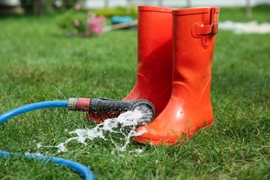 Photo of Orange rubber boots under water pressure on green grass outdoors