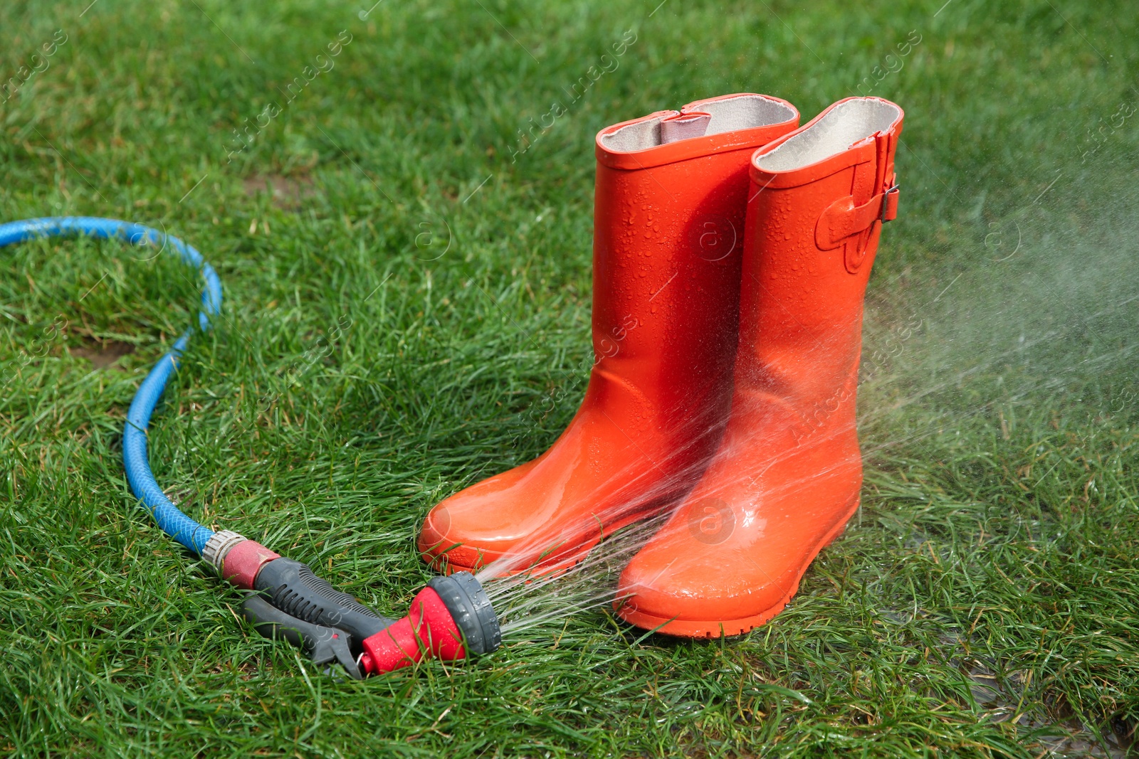 Photo of Orange rubber boots under water pressure on green grass outdoors