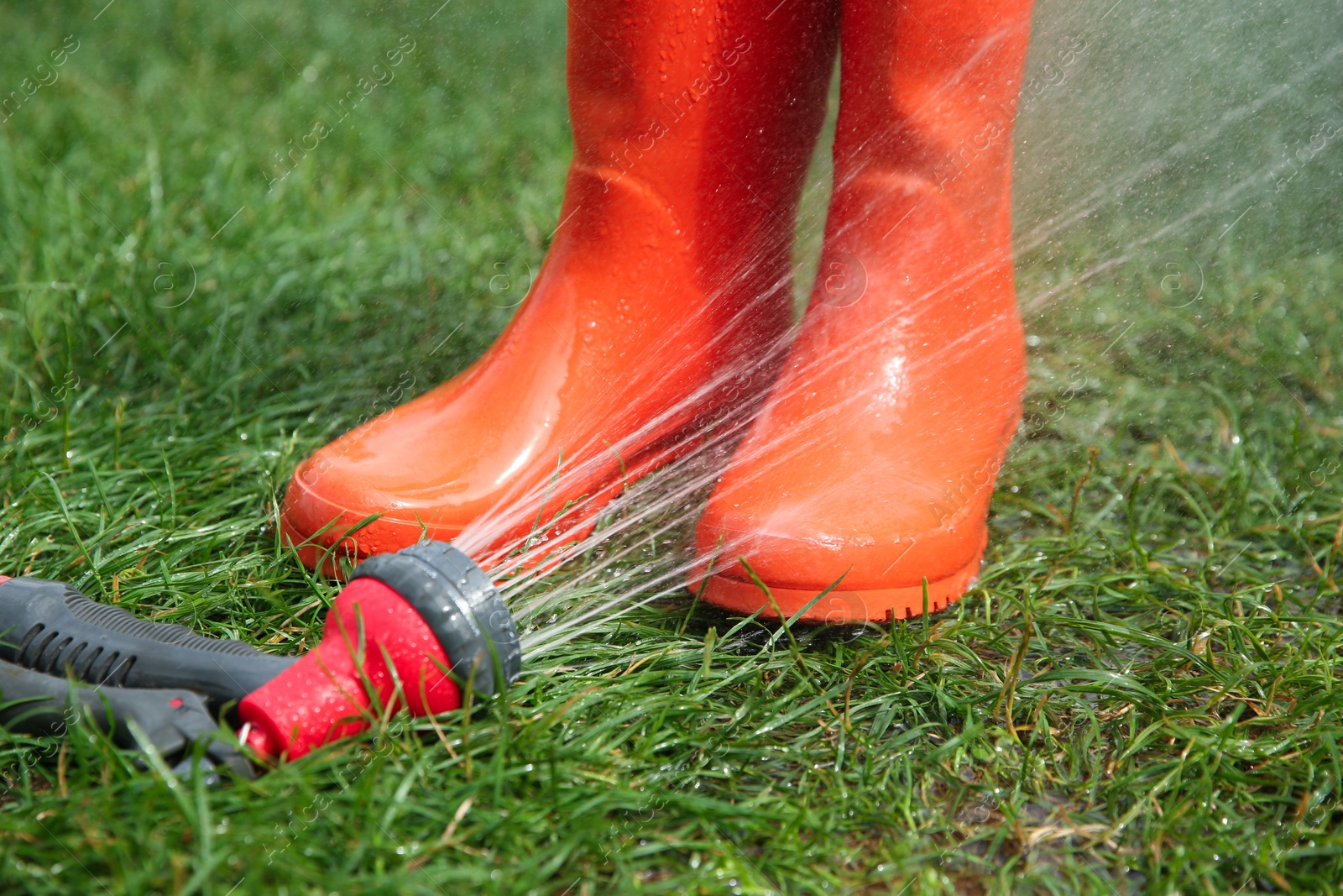 Photo of Orange rubber boots under water pressure on green grass outdoors