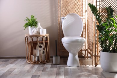 Photo of White toilet bowl, paper rolls and houseplants in bathroom