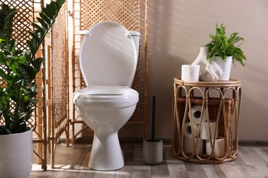 Photo of White toilet bowl, paper rolls and houseplants in bathroom