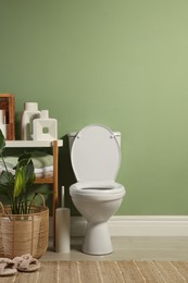 Photo of White toilet bowl, paper rolls, slippers and houseplants in bathroom